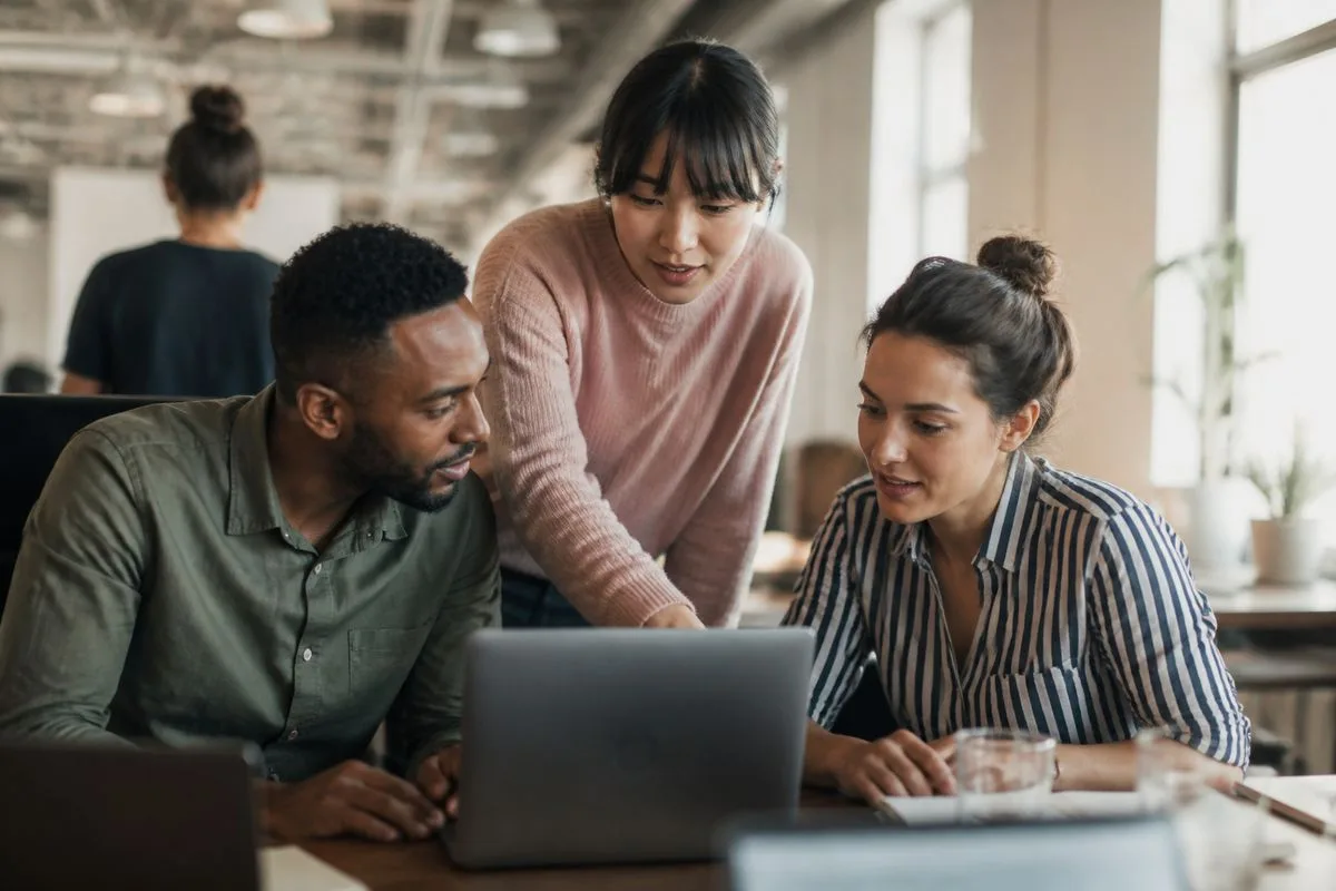 Employees collaborating around laptops in a modern office.