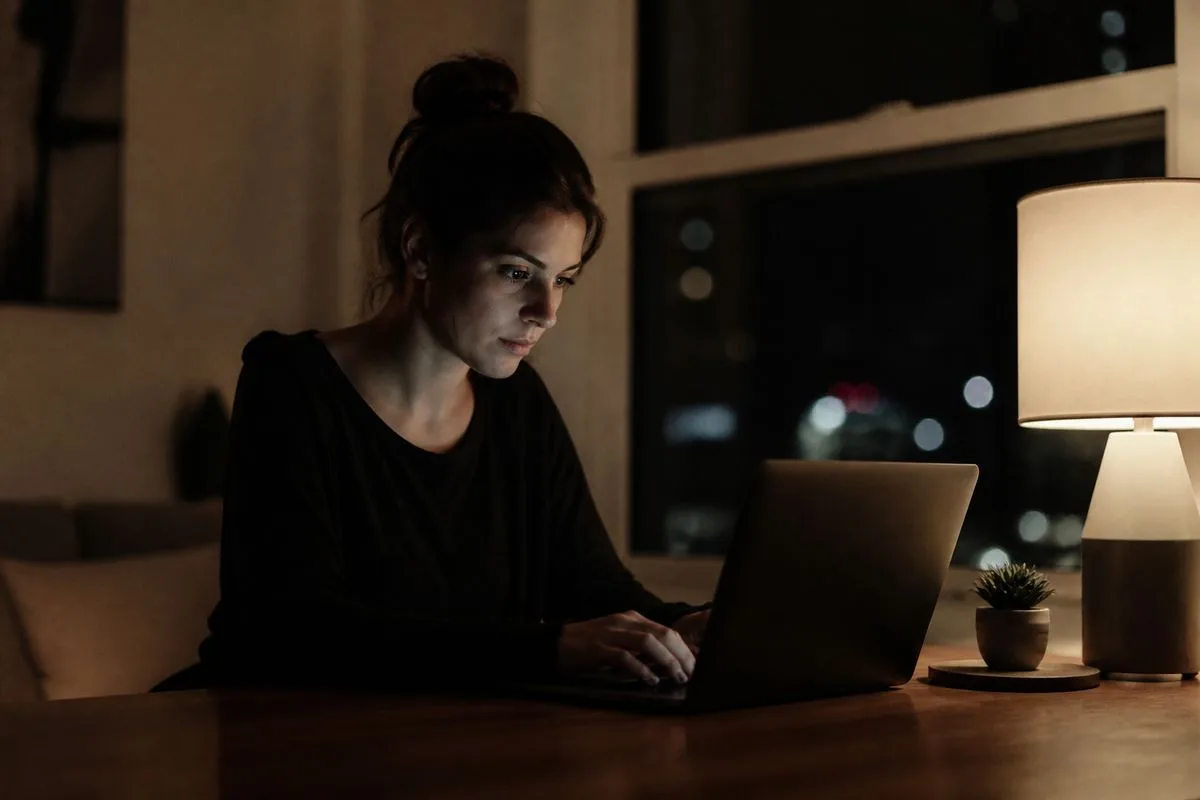 A woman sitting alone, typing on a laptop late at night