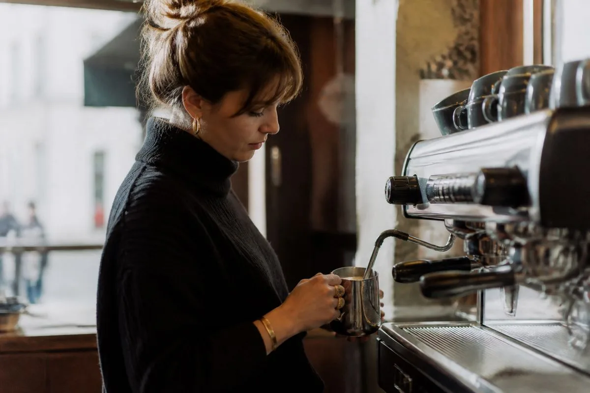 A barista preparing coffee with a De Longhi machine and milk frother