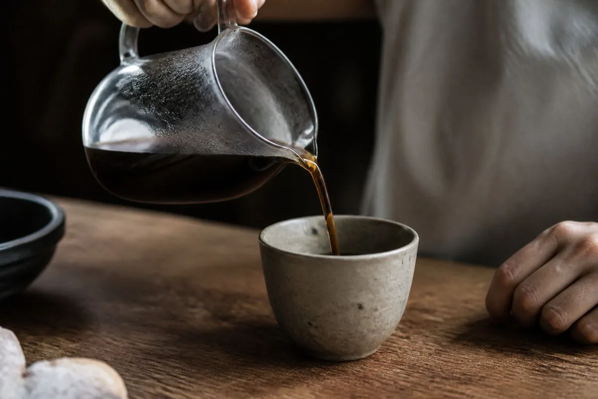 Close-up of a hand pouring coffee from a glass carafe