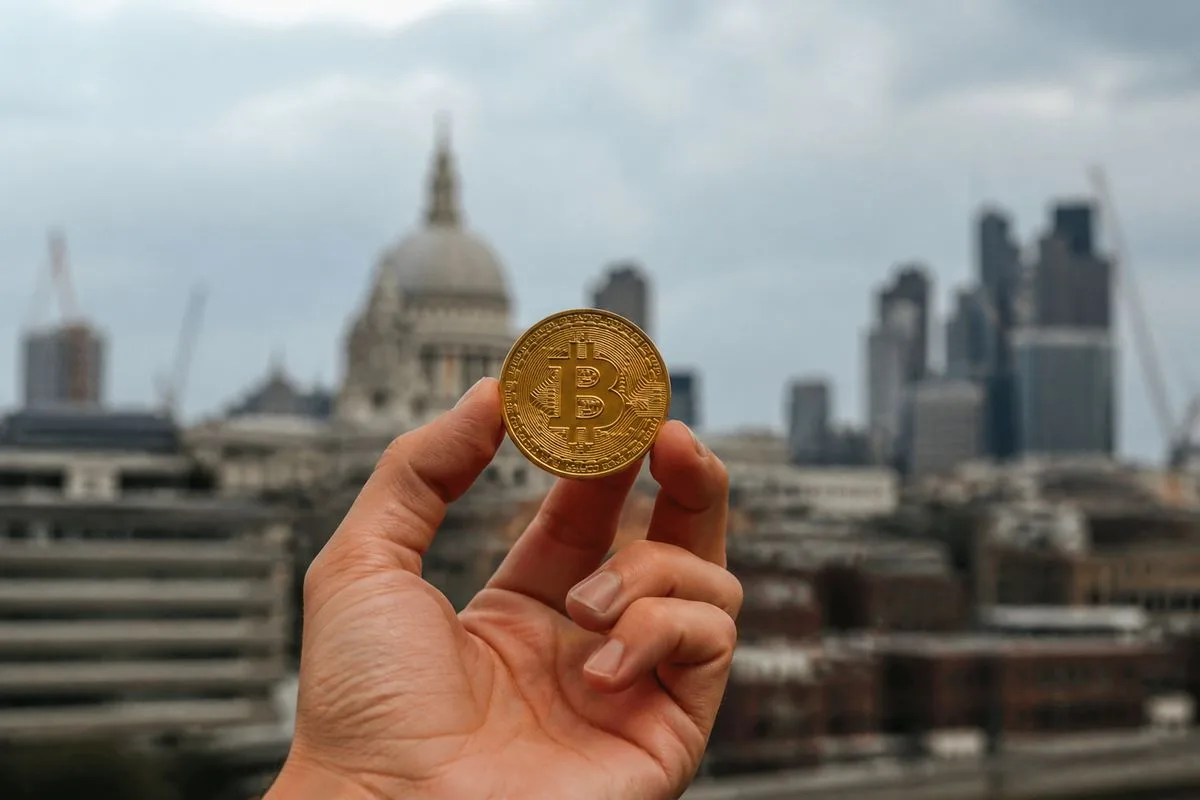 A person holding a physical Bitcoin coin against a city backdrop