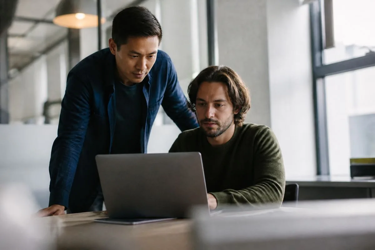 Sales engineers collaborating over a laptop in a modern office.