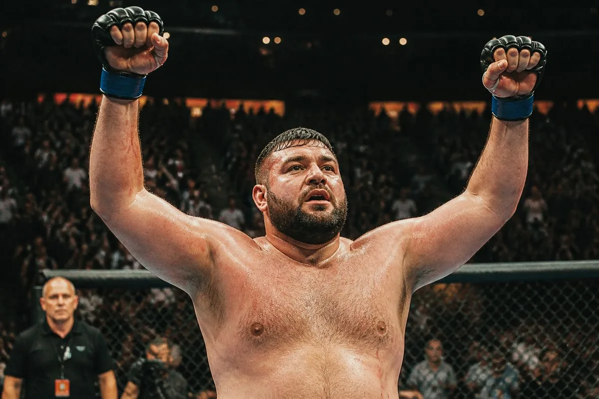 A victorious heavyweight fighter raising his arms in the octagon