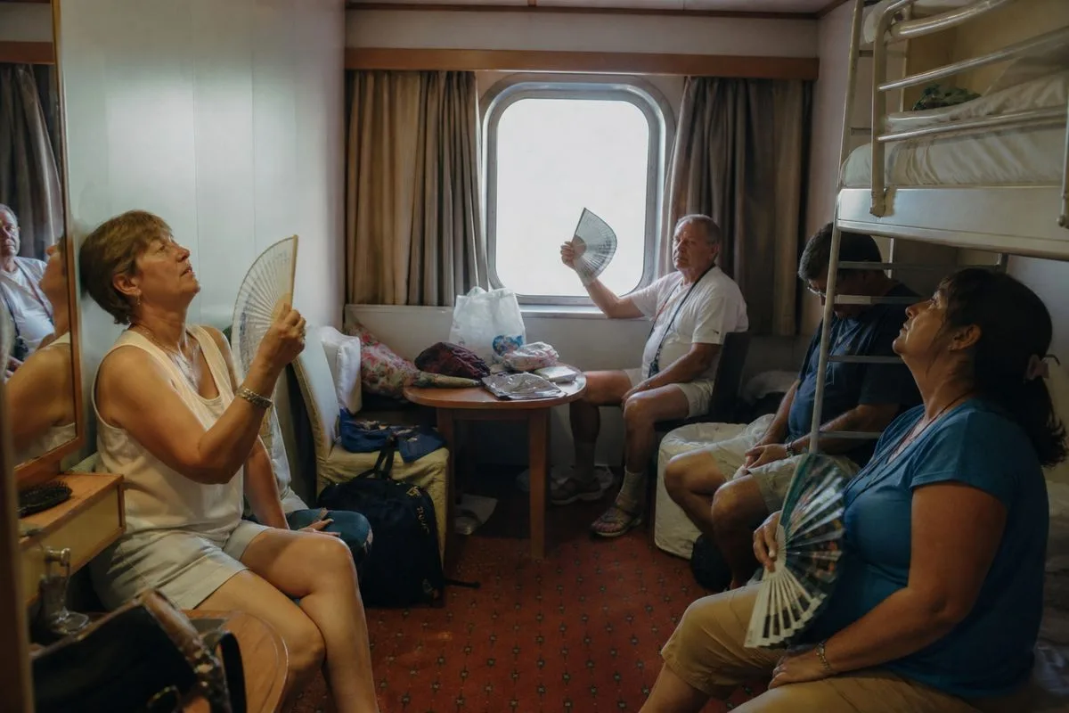 Passengers fanning themselves inside a cramped cruise ship cabin.