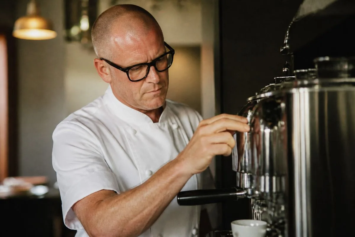Heston Blumenthal adjusting a sleek coffee machine in kitchen