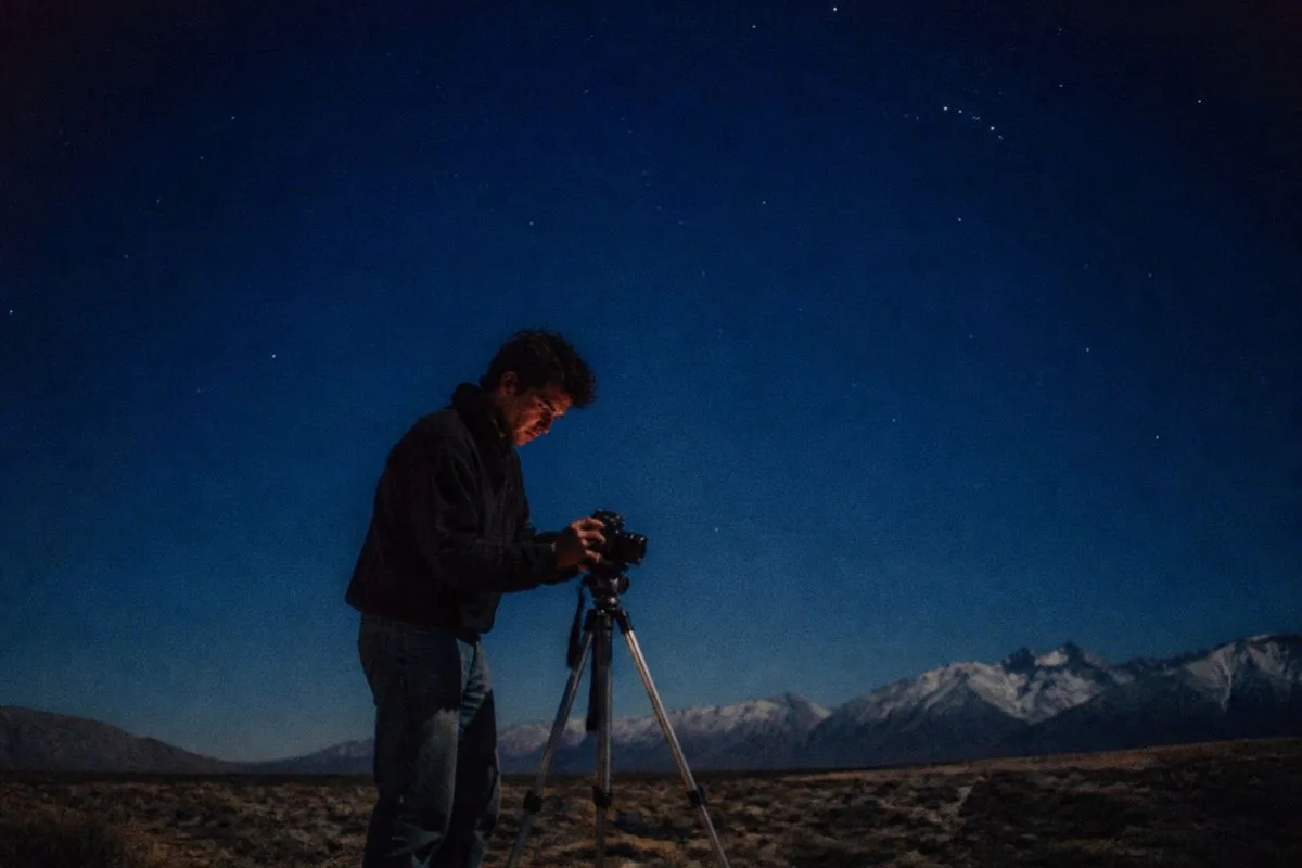 A person setting up a camera under a dark, clear night sky.