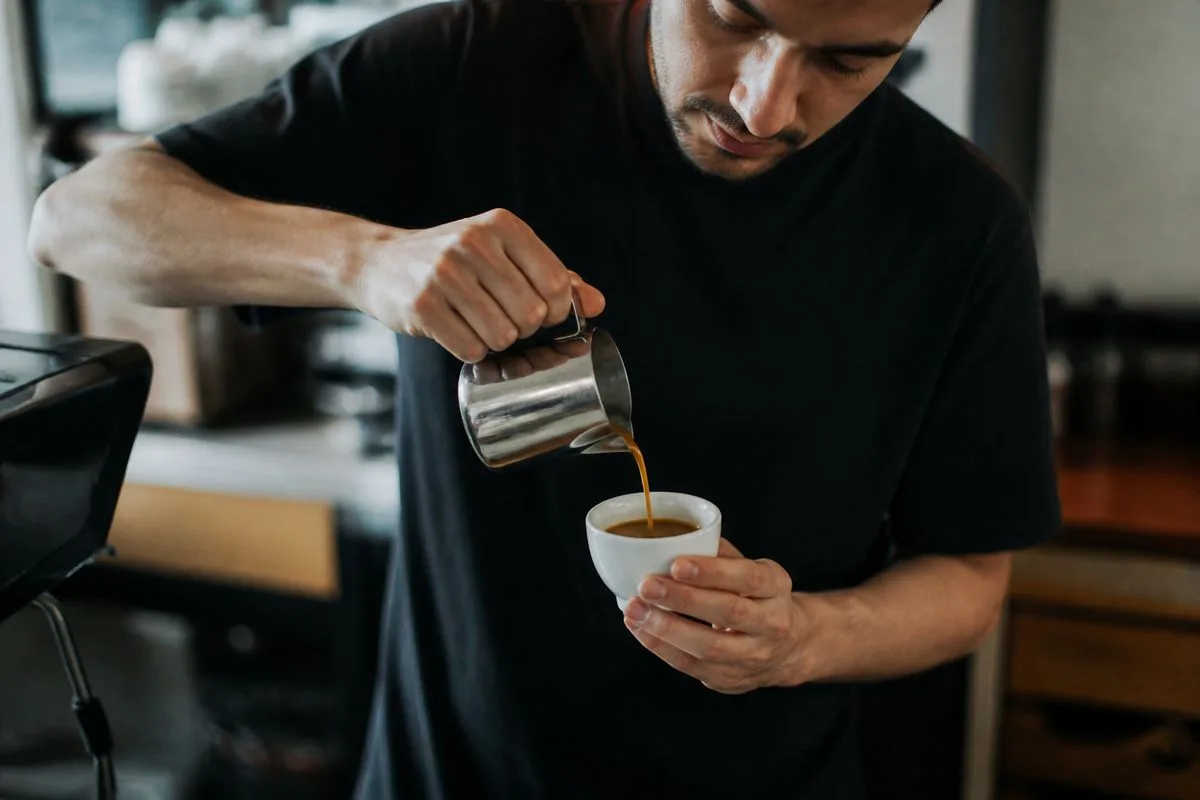 A barista pouring dark espresso into a small cup.