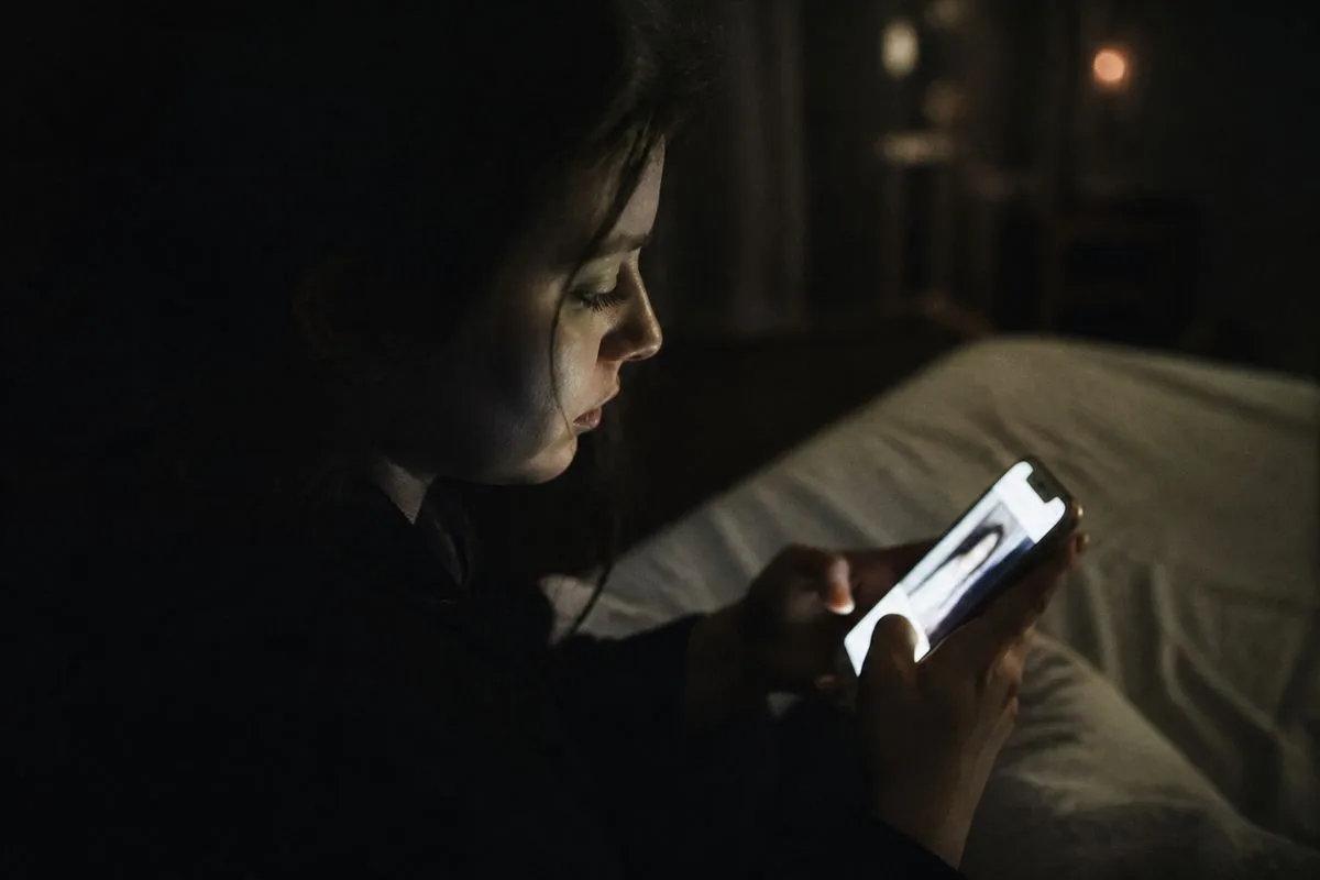 A person scrolling social media on a smartphone in dim light