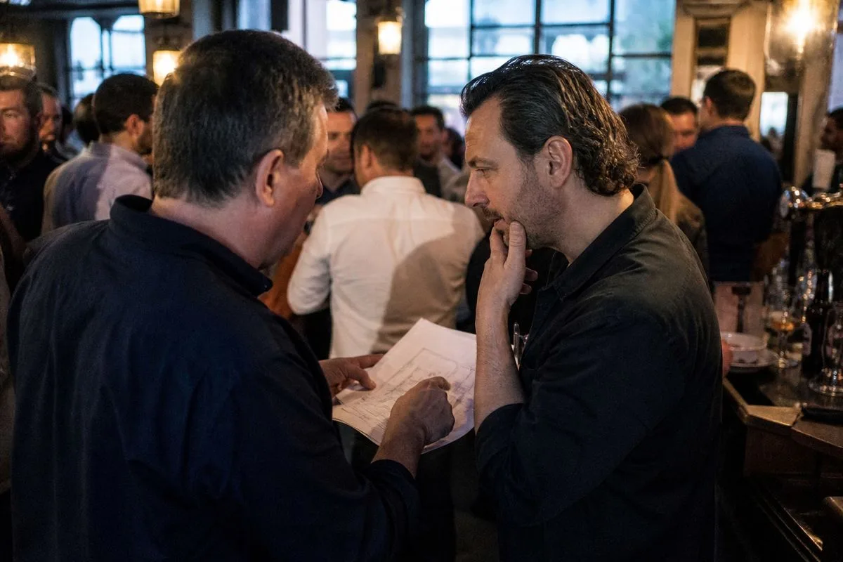 Pub owners discussing plans inside a crowded bar.