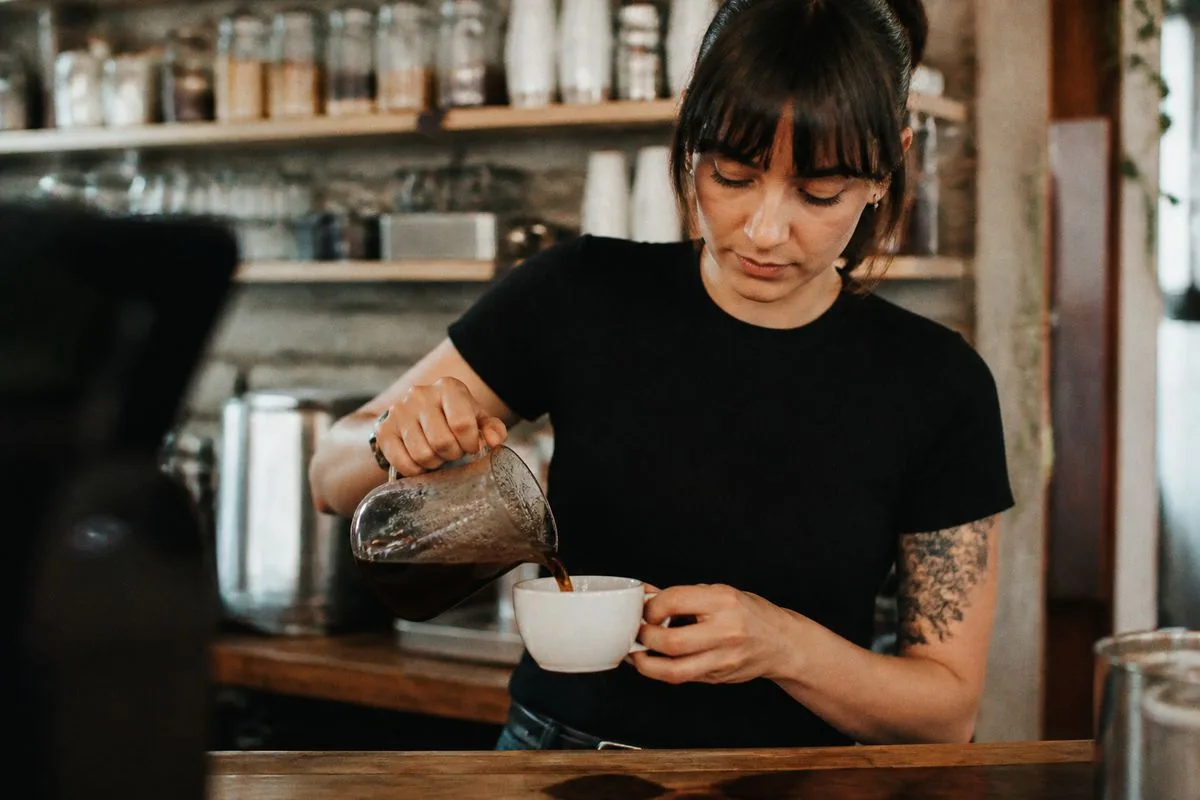 A barista pouring dark roast coffee into a cup