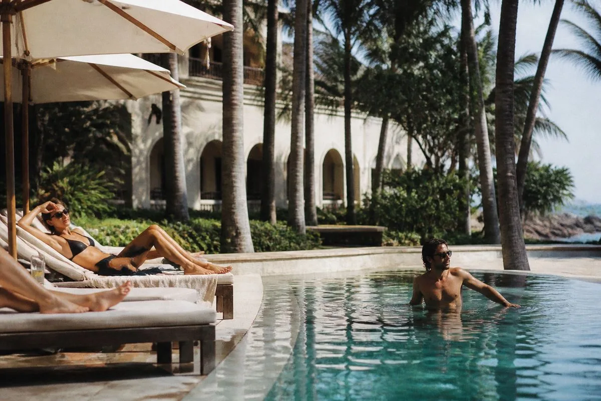 Guests lounging by a hotel pool under palm trees
