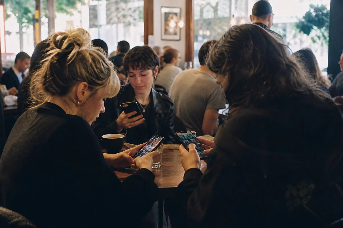 Fans scrolling concert listings on smartphones in a crowded café