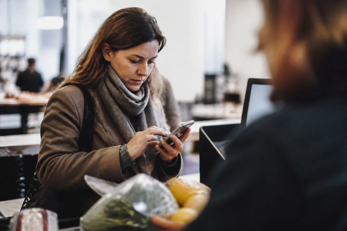 A shopper hurriedly using a smartphone at a store checkout