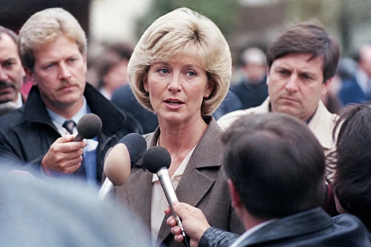 Karen Barber speaking at a press conference with reporters nearby