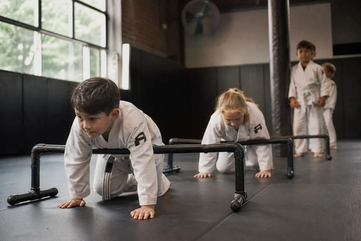Children in martial arts uniforms practicing drills at Omne MMA gym