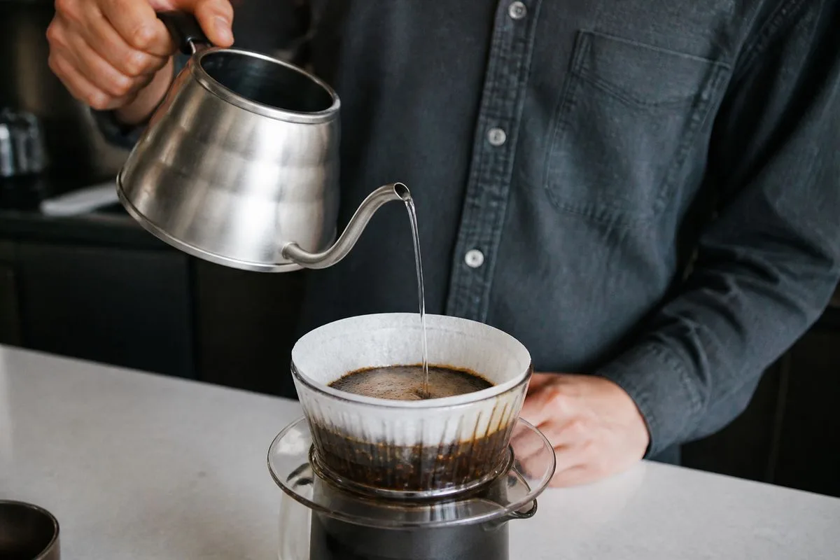 A person pouring hot water over coffee grounds in a flat-bottom dripper