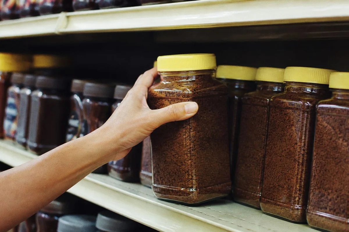 A hand reaching for a jar of Café Bustelo instant coffee on a store shelf